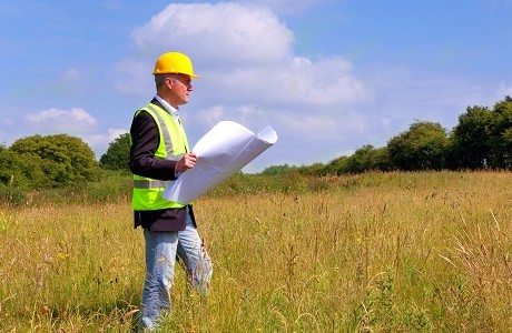 Architect in a field looking at architectural plans representing Restrictive Covenants Indemnity Insurance