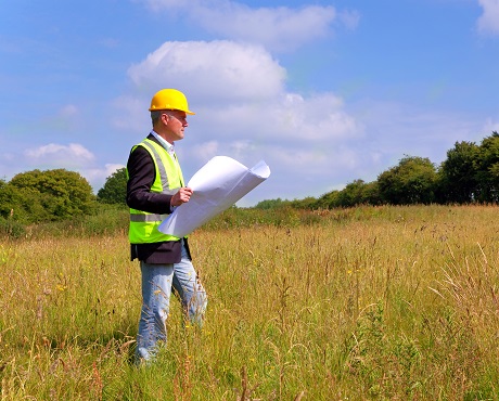 Architect in a field looking at architectural plans representing Restrictive Covenants Indemnity Insurance