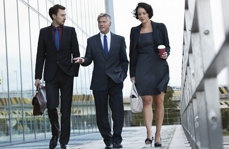 Three businesspeople walking and talking next to an office building representing professional associations