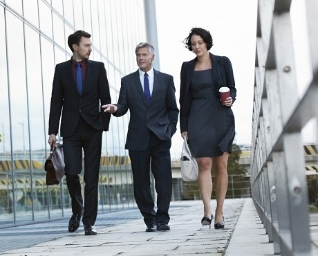 Three businesspeople walking and talking next to an office building representing professional associations